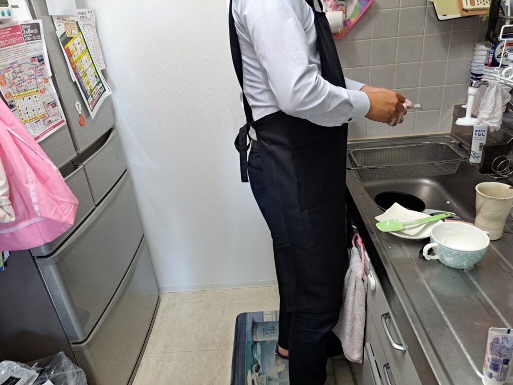 カスタムデザインエプロンを着用し洗い物をしている男性