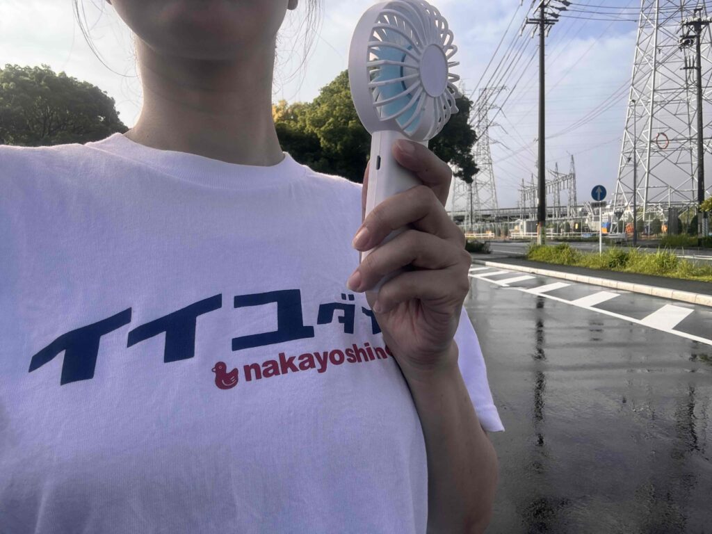 充電式ハンディファンを手に持って外を歩いている女性
