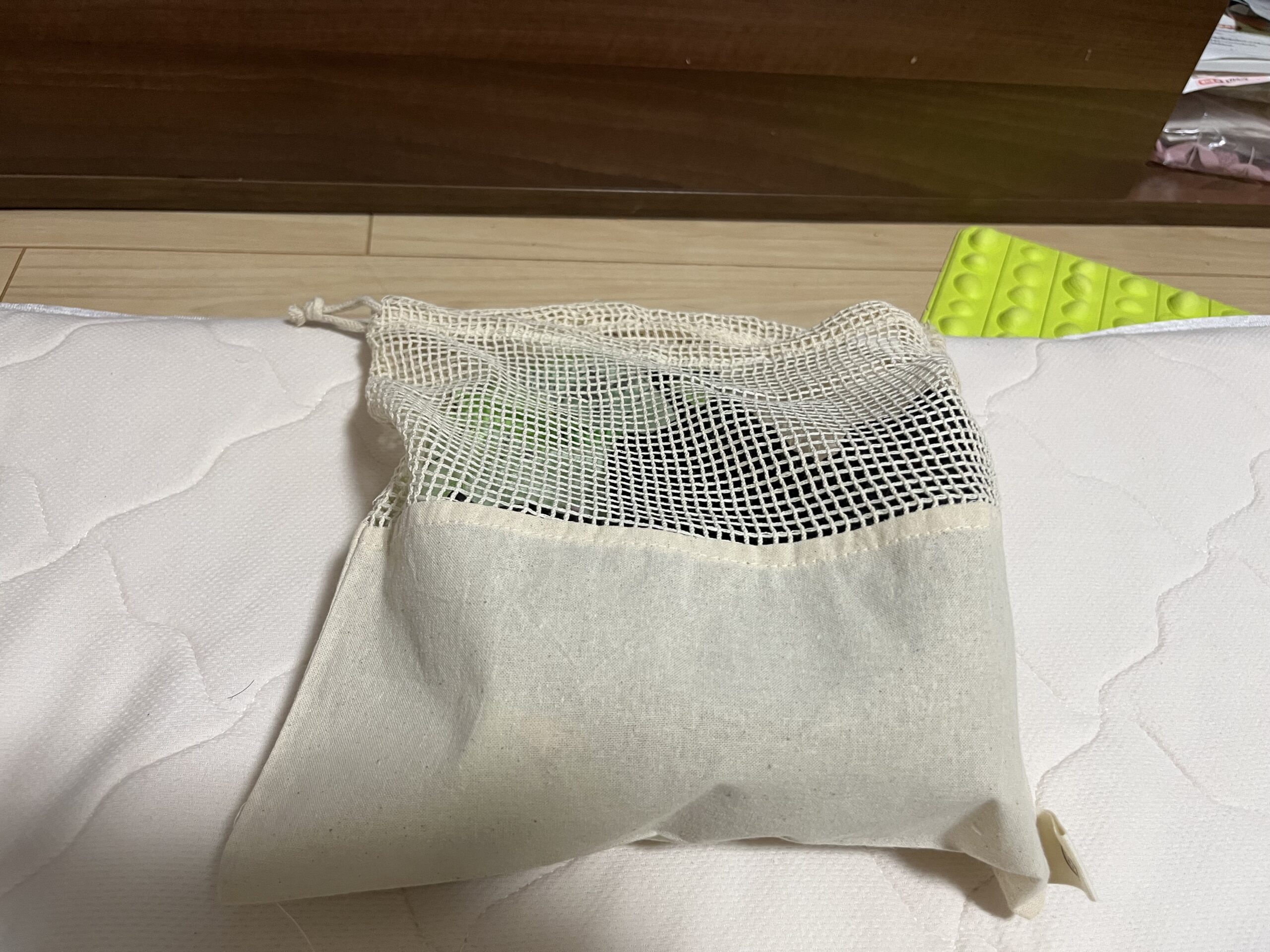 オーガニックコットンネット巾着（L）　ナチュラルに着替えを入れて床に置いた様子