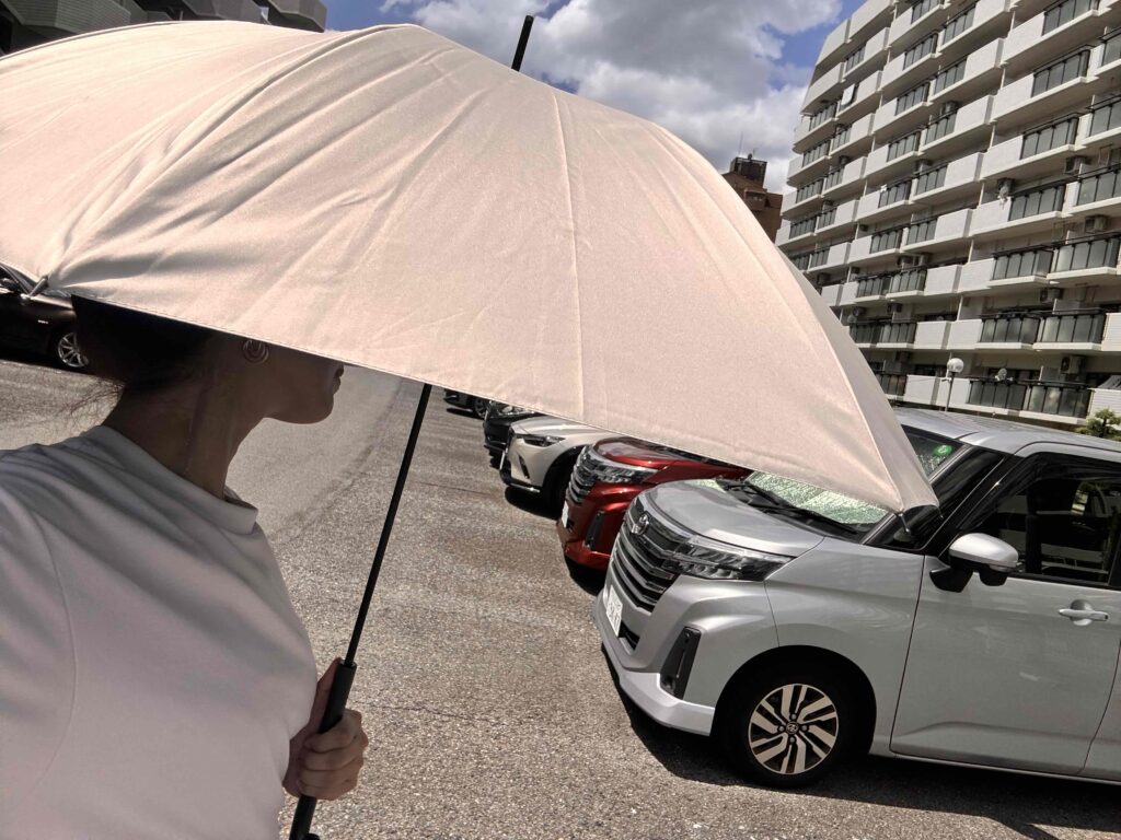 遮光長傘を差して駐車場を歩く女性