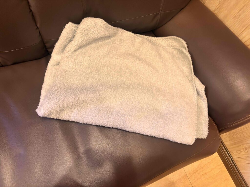 カチオン染めレギュラーブランケット（巾着付）グレーがたたまれてソファーに置いてある
